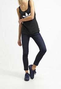 Svart ärmlös linne med vitt logo, parat med mörkblå tajta jeans och marinblå snörskor med uppvikta ärmar.