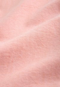 Gros plan sur un tissu rose doux et texturé avec un tissage visible et des plis légers créant des variations de lumière et d'ombre.