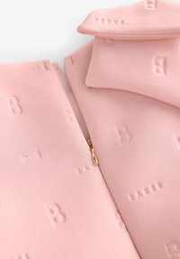 Rosa tyg med präglade bokstäver och ett mönster av rosetter, med en gulddetalj på dragkedjan. Slät textur, hopvikta och överlappande bitar.