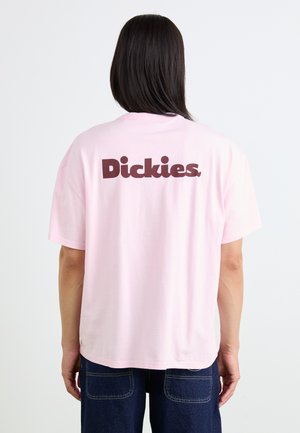 Lyserød bomulds t-shirt med korte ærmer og rundet kant. Stort mørkebrunt "Dickies"-logo trykt på ryggen. Ingen mønstre eller dekorationer synlige.
