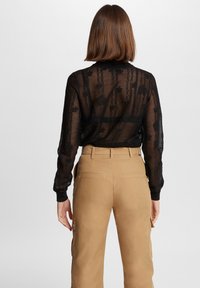 Zwart doorschijnend top met een textuurpatroon, lange mouwen, gecombineerd met beige cargo pants, voorzien van zakken en een gladde stofafwerking.