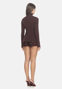Brauner gerippter Rollkragenpullover kombiniert mit burgunderfarbenen Pailletten-Shorts und High-Heels, zeigt ein figurbetontes Design und texturierten Stoff.