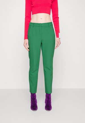 Pantalons ajustés verts avec une texture lisse, présentés avec un devant plat et des poches latérales. Assortis à un haut court rouge vif et à des bottines violettes.