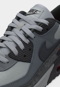 Κοντινό πλάνο γκρι αθλητικού παπουτσιού Nike που δείχνει υφασμένες κορδόνια, πάνελ από δίχτυ και δέρμα, μαύρο λογότυπο swoosh και ορατό αερόσακο στην σόλα.
