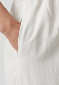 Lightweight white linen fabric drapes smoothly, featuring a side seam pocket and subtle texture from woven fibers.