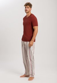Roodbruin T-shirt met korte mouwen en V-hals, gecombineerd met lichtgrijze pyjamabroek met verticale maroon en crèmewitte strepen. Blote voeten.