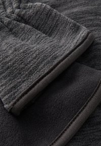 Kullgrå fleece-stof med en tekstureret overflade, lagd over et glat sort stof. Kanterne har en mørk elastisk kant.