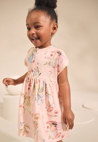 Rózsaszín ruha rövid ujjakkal, színes tündér- és virágmintákkal díszítve. Az anyag puha tapintású, a szoknya redőzött kialakítású.