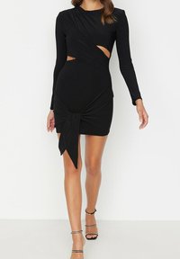 Abito nero a maniche lunghe con dettagli a taglio, nodo in vita, silhouette aderente, realizzato in tessuto liscio, lunghezza fino a metà coscia.