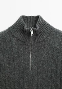 Maglione grigio a maglia con colletto alto a costine e zip di metà lunghezza. Presenta un motivo a treccia texturizzato su tutta la superficie.