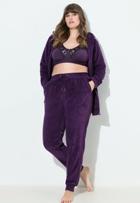 Violetti samettitrainingsuit, jossa on huppu ja nyöripantsit; pehmeä rakenne, rento istuvuus ja hienot yksityiskohdat rintaliiveissä. Ihanteellinen kotioloihin.