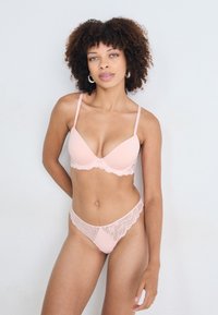 Rosa bh och stringset har en slät, vadderad design med delikata spetsdetaljer längs kanterna. Justerbara axelband förbättrar passformen.