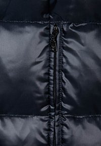 Námořnická modrá péřová bunda s hladkou, lesklou texturou, vertikálně prošívanými sekcemi a centráln ím černým zipem.