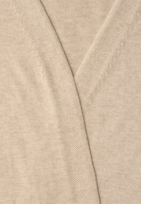 Gros plan sur un tissu beige en tricot avec une couture en forme de V et une fine texture de points.