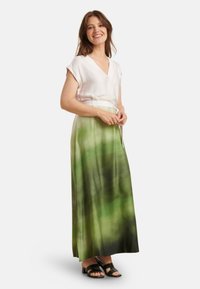 Maxi rok in een vervagend groen patroon met een vloeiende ontwerp, gecombineerd met een witte blouse en zwarte sandalen. Glad stofoppervlak.