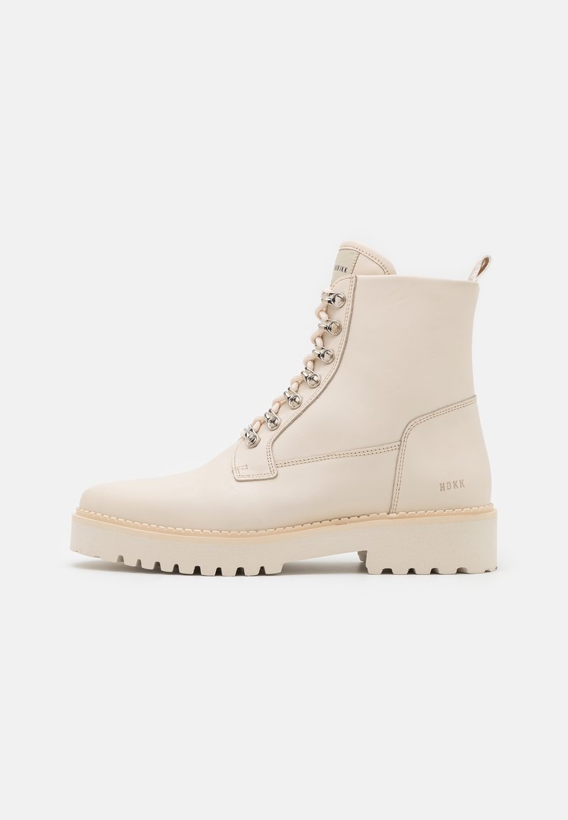 Bottine en cuir couleur crème avec semelle épaisse, œillets métalliques, laçage avant, et logo « MBKK » sur la partie talon.