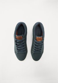 Sapatilhas azul-escuras em material de camurça suave, com design de bico redondo, seis ilhós e detalhes em couro castanho com um rótulo de marca.