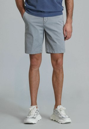 Light gray cotton shorts with side pockets, rolled cuffs, and a clean design. Paired with chunky white sneakers featuring a gray pattern.