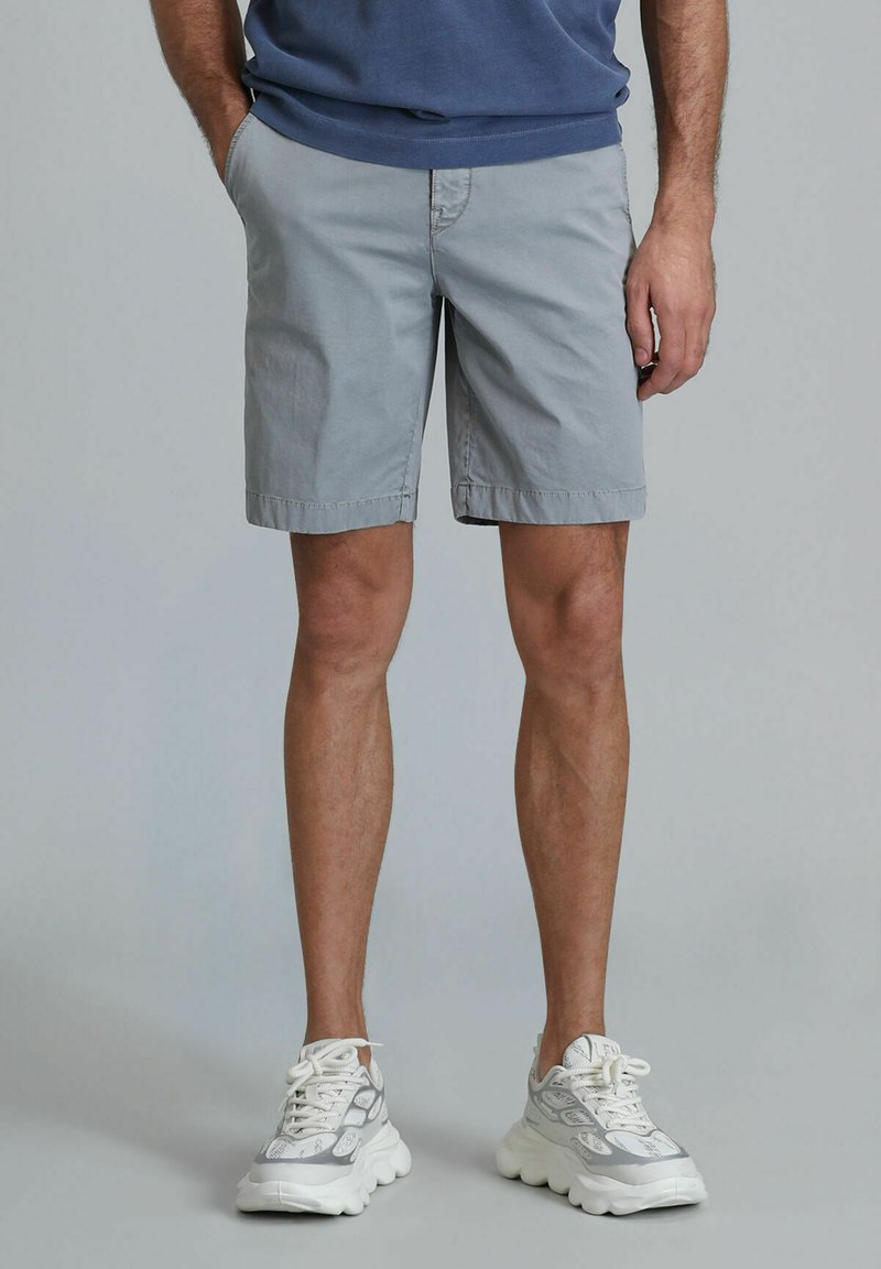 Helle graue Baumwollshorts mit Seitentaschen, umgeschlagenen Säumen und einem schlichten Design. Kombiniert mit klobigen weißen Sneakers mit grauem Muster.