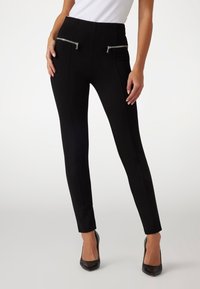 Black ankle-length pants made of stretchy material featuring two zippered front pockets, a high waistband, and a slim fit.