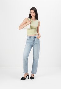 Light green fitted tank top, high-waisted light blue jeans, black heeled slingback shoes with bow detail, carrying a small white bag.
