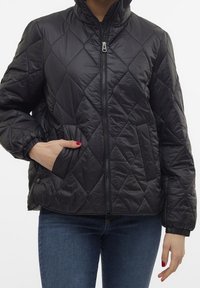 Veste noire matelassée avec fermeture éclair à l'avant, col montant et poignets élastiques. Comprend des poches latérales et une texture douce et brillante.