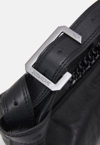 Sort lædertaske rem med en sølvfarvet geometrisk spænde. Har tekstureret syning og et signaturlogo detail.