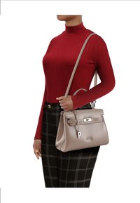 Graue Lederhandtasche mit strukturiertem Design, silberner Hardware und abnehmbarem Anhänger, getragen an einer Schulter mit einem langen Riemen.