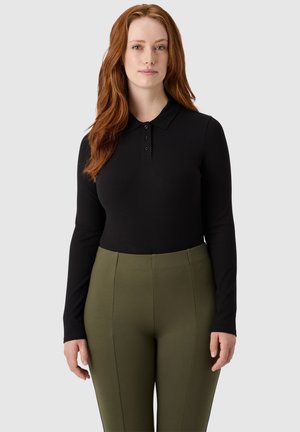 Polo nero a maniche lunghe con texture a coste e pattina con tre bottoni, abbinato a pantaloni verdi oliva a vita alta con dettagli di cucitura.