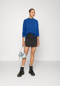 Niebieski dzianinowy sweter, czarna mini spódniczka z bocznym rozcięciem, czarne buty za kostkę z sznurówkami oraz mała iryzująca torebka.