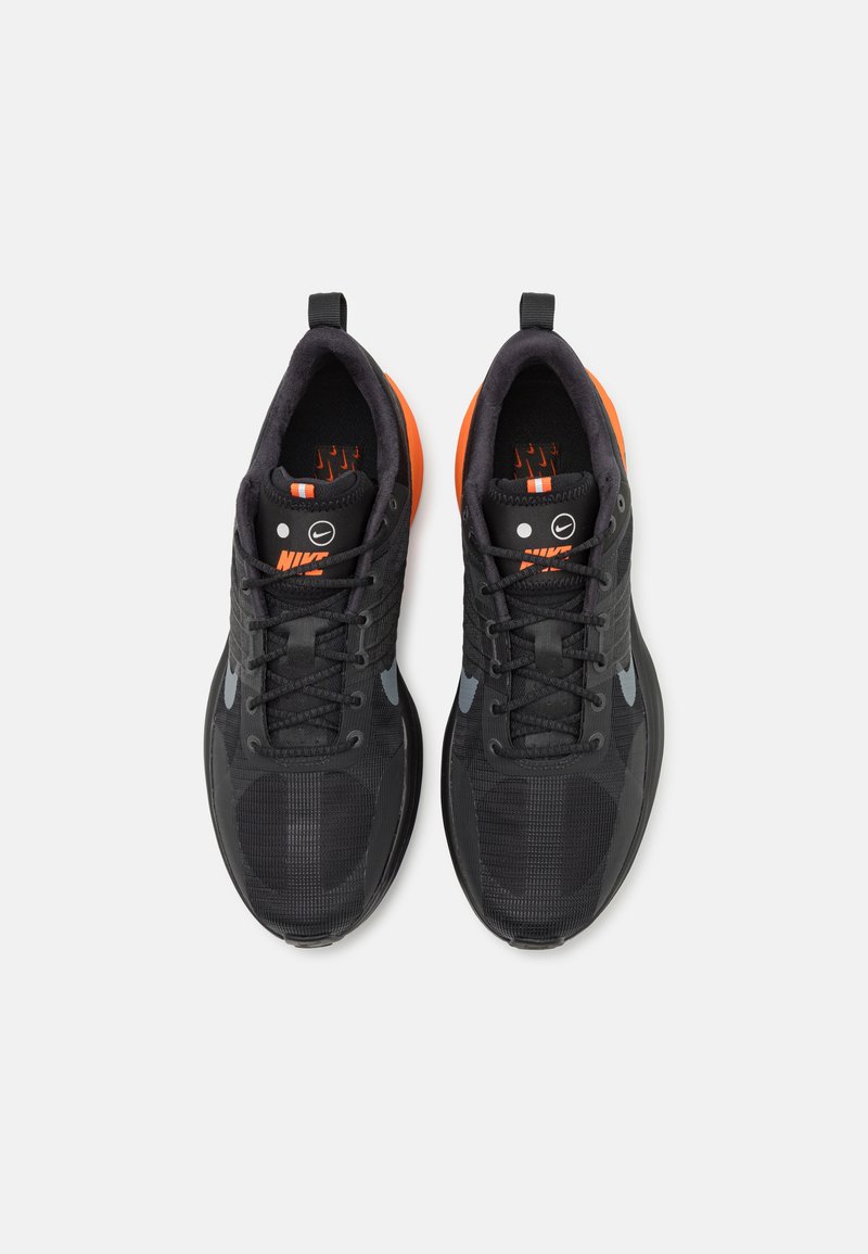 Para czarnych butów do biegania Nike z pomarańczowymi piętami, szarymi logo swoosh i czarnymi sznurowadłami, pokazanych z góry na białym tle.