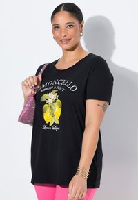 Camiseta negra con un diseño gráfico de limones y flores, combinada con pantalones rosas y un bolso rosa brillante.