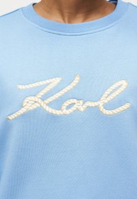 Φωτεινό γαλάζιο φούτερ με τη λέξη "Kal" κεντημένη με παχύ, στριφτό λευκό νήμα σε στυλ σχοινιού στο στήθος.