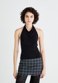 Μαύρο τοπ με δέσιμο στον λαιμό και ριχτό ντεκολτέ, συνδυασμένο με γκρι καρό μίνι φούστα. Το σύνολο περιλαμβάνει δαντελωτές καλσόν για επιπλέον υφή.