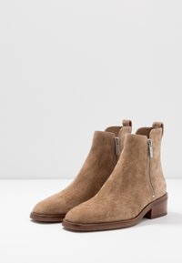 Brązowe zamszowe botki za kostkę z zaokrąglonym noskiem, bocznymi suwakami i niskimi słupkowymi obcasami. Gładka tekstura i minimalistyczny design bez widocznych wzorów.