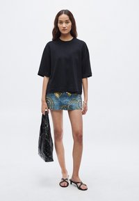 Čierne oversize tričko, roztrhaná džínová minisukňa s kovovými cvokmi a vzormi, čierne sandále a lesklá čierna kabelka tote.