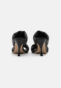 Sapatos de salto alto em couro preto com traseira arredondada e suave, e um salto esguio, apresentando um design de parte superior aberta e textura lisa.