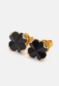 Brincos em tom de ouro apresentando um design de trevo de quatro folhas com pedras negras facetadas, exibindo superfícies brilhantes e bordas suaves.