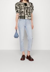 Top negro y crema con mangas abullonadas y patrones geométricos, combinado con jeans rectos de color azul claro y mocasines marrones. Pequeño bolso azul.