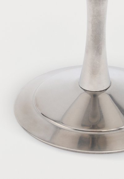 Sijajna kovinska okrogla podlaga s cilindričnim steblom v sredini na belem ozadju.