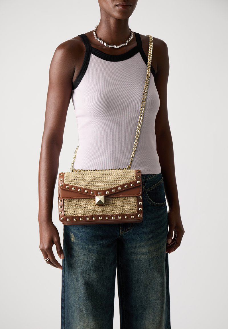 Sac à main en paille tissée beige avec des accents en cuir marron, des garnitures en or et des détails cloutés, doté d'une bandoulière en chaîne et d'une fermeture rabat.