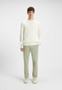 Maglione bianco a coste, pantaloni verde chiaro e sneaker beige. Il maglione ha un collo a giro e l'outfit ha una vestibilità rilassata.