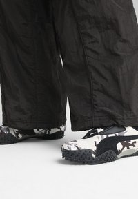 Puma sneakers met een zwart-wit camouflagedesign, gestructureerde rubberen zolen en zwarte accenten. Draag ze met losse zwarte broeken.