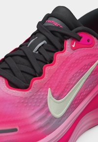 Κοντινό πλάνο ροζ αθλητικού παπουτσιού Nike με μαύρα κορδόνια, λευκό λογότυπο Nike και υφή στο επάνω μέρος κοντά στις τρύπες για κορδόνια και τη γλώσσα.