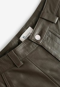 Donkergroene leren broek met een gladde textuur, een knoopsluiting en een label met de tekst "N. PREMIUM COLLECTION." Gedetailleerde stiksels zichtbaar.