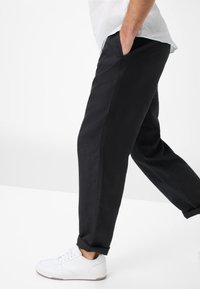 Zwarte linnen broek met een relaxte pasvorm, voorzien van zijzakken en opgerolde mouwtjes, gecombineerd met witte sneakers.