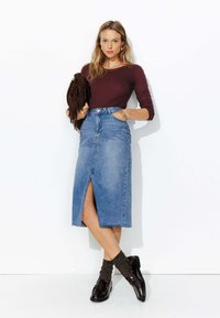 Jupe maxi en denim avec une fente devant, assortie à un haut ajusté à manches longues bordeaux et des mocassins foncés avec des chaussettes texturées.