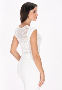 Weißes Strickoberteil mit kurzen Ärmeln, das eine gemusterte Textur und eine figurnahe Passform aufweist. Rückansicht, die das offene Strickmuster zeigt.