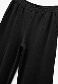Pantalons de survêtement noirs avec une taille élastique, des poches latérales, une texture lisse et une coupe décontractée. Design classique sans motifs ni accents.
