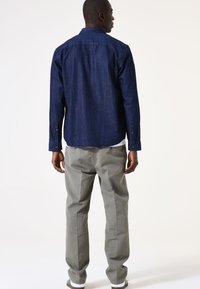 Camisa de denim en azul oscuro con cuello abotonado y mangas largas, combinada con pantalones gris claro y zapatillas blancas.
